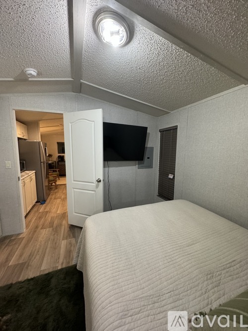 A bedroom with a bed, a television, and a refrigerator in the kitchen area.