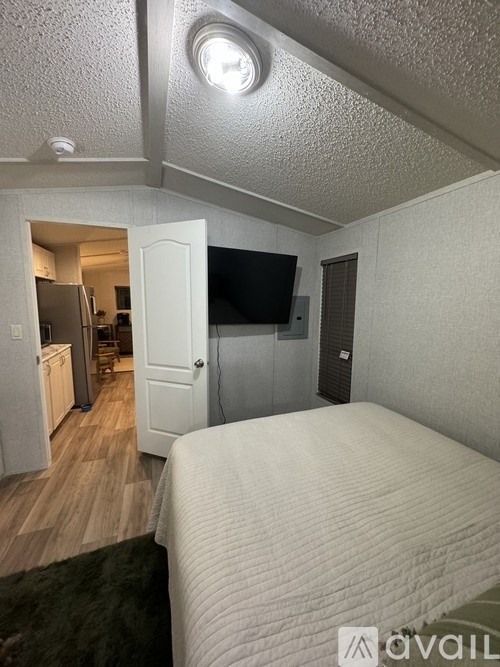 A bedroom with a bed, a television, and a refrigerator in the kitchen area.