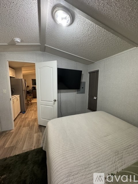 A bedroom with a bed, a television, and a refrigerator in the kitchen area.