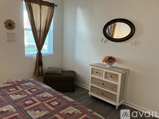 A bedroom with a bed, a dresser, and a window with curtains.