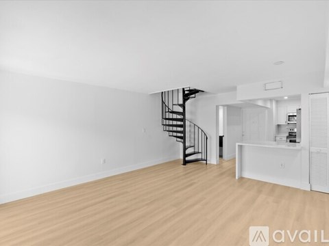 A spacious room with wooden flooring and a black spiral staircase.