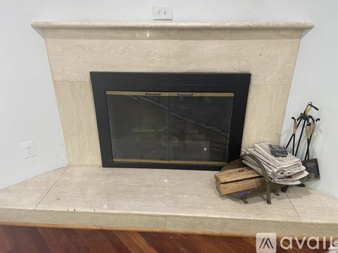 A fireplace with a black screen door and a stack of magazines on a wooden stand.