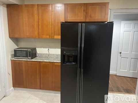 A black refrigerator stands in a kitchen with wooden cabinets.