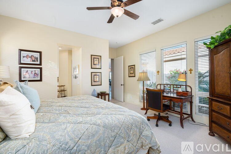 A bedroom with a bed, a desk, and a ceiling fan.