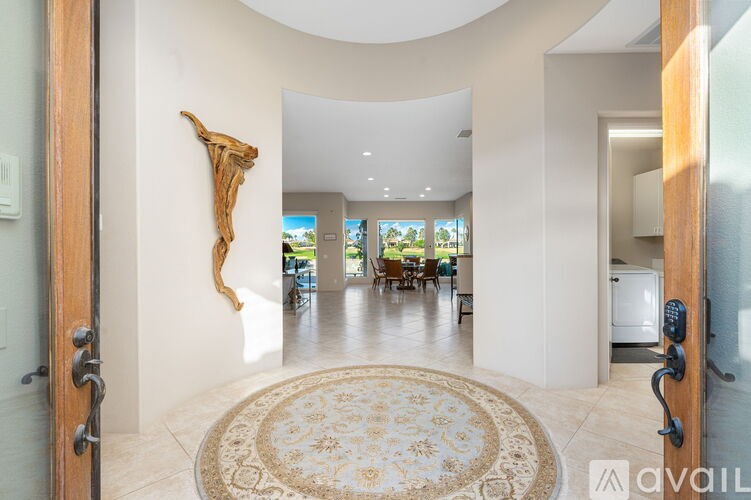 A large, open living room with a rug in the middle and a sculpture on the wall.