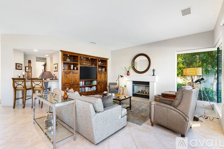 A living room with a grey couch, a glass coffee table, a fireplace, and a bookshelf.