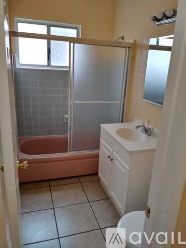 A bathroom with a pink tub, white sink, and a window.