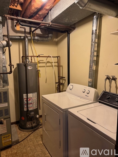 A washer and dryer in a small room with a water heater and pipes.