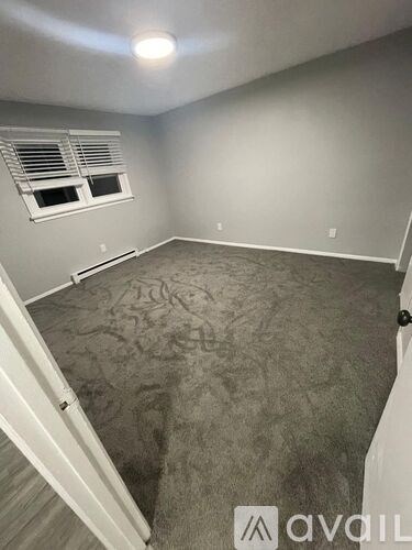 A room with a carpeted floor and a window with blinds.