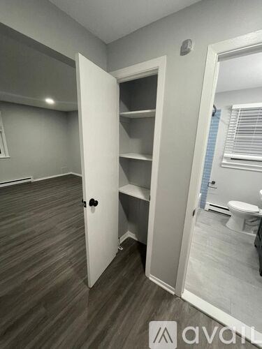 A room with a white door and a toilet in the background.