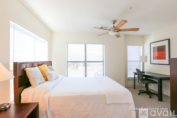 A bedroom with a bed, desk, and window with blinds.