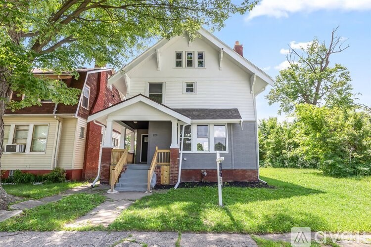 A two-story house with a front porch and a tree in front.