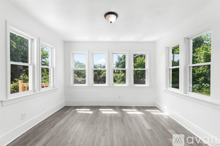A spacious room with white walls and wooden flooring, featuring a large window with a view of trees.