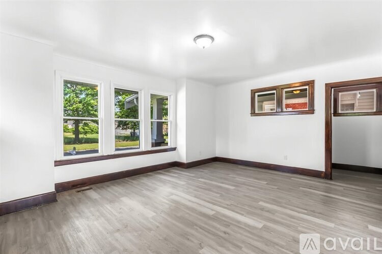 A room with wooden flooring and three windows.
