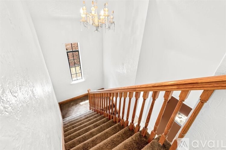 A staircase with a wooden railing and a chandelier in a white room.