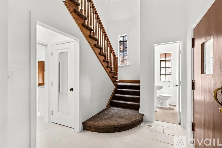 A staircase with a brown carpeted runner leads up to a white door.