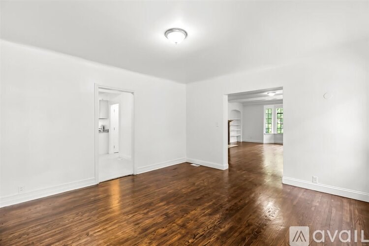 A room with wooden floors and white walls, with a door on the left and a window on the right.