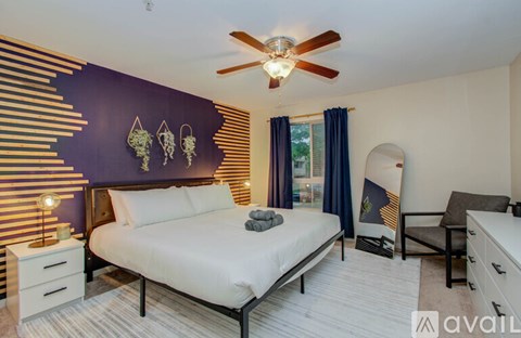 A bedroom with a bed, a ceiling fan, and a wall decoration.