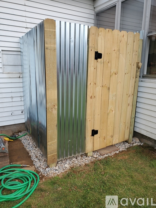 A green hose is laying on the grass next to a wooden and metal shed.