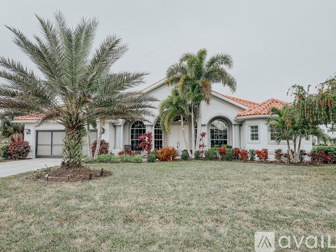 A white house with a red roof and a palm tree in front.