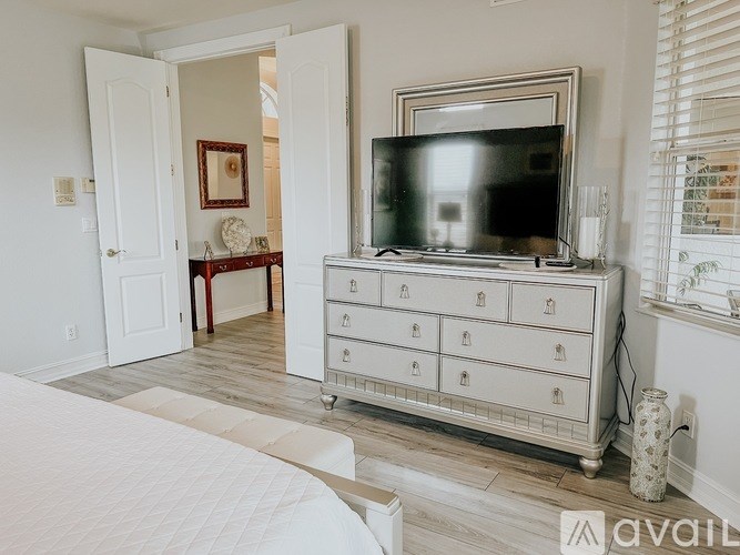 A white bedroom with a bed, dresser, and television.