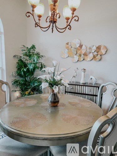 A dining table with a glass top and a chandelier hanging above it.