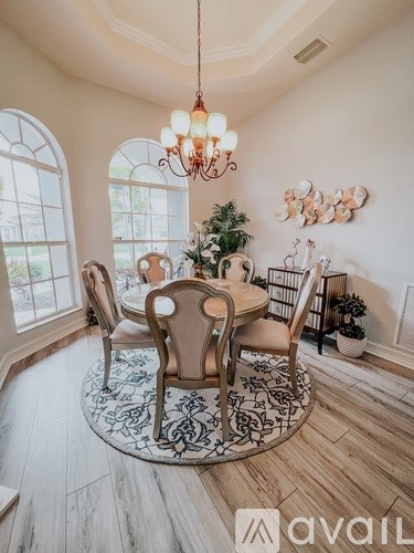 A dining room with a round table and chairs, a chandelier, and a plant.