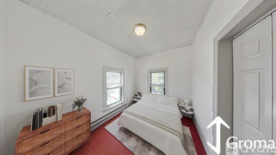 A bedroom with a white bed and a wooden dresser.
