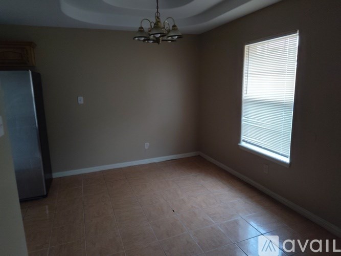 A room with a fridge, a window with blinds and a chandelier.