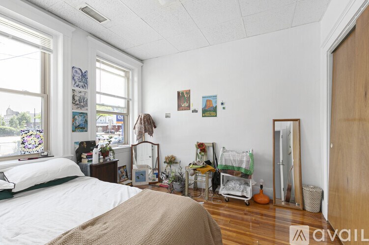 A bedroom with a bed, dresser, mirror, and a window with a view of the street.