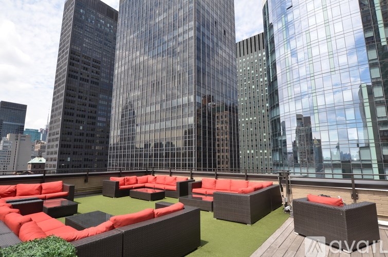 A rooftop patio with red couches and black tables overlooks a city skyline.
