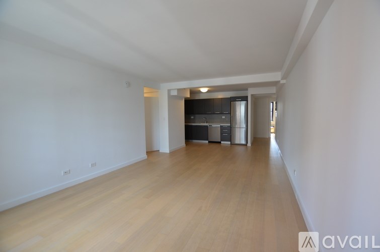 A room with wooden floors and white walls, leading to a kitchen area.