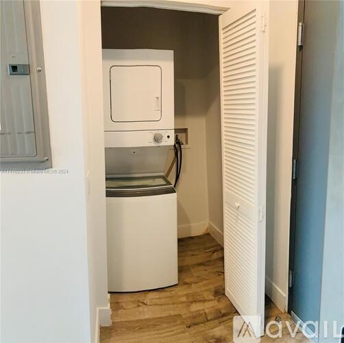 A small white washing machine is in a narrow space between a wall and a cabinet.