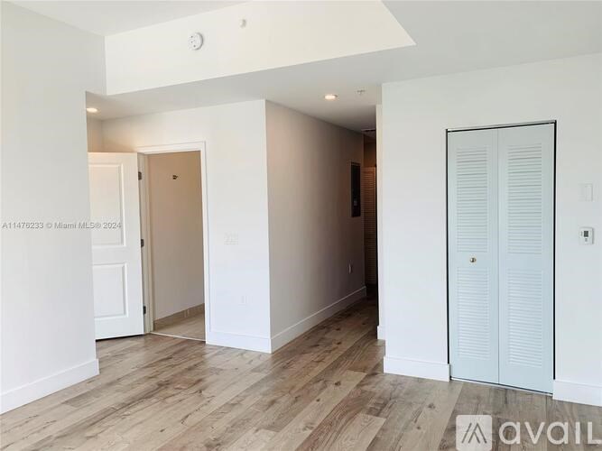 A room with white walls and wooden flooring, with a door on the left and a white wardrobe on the right.