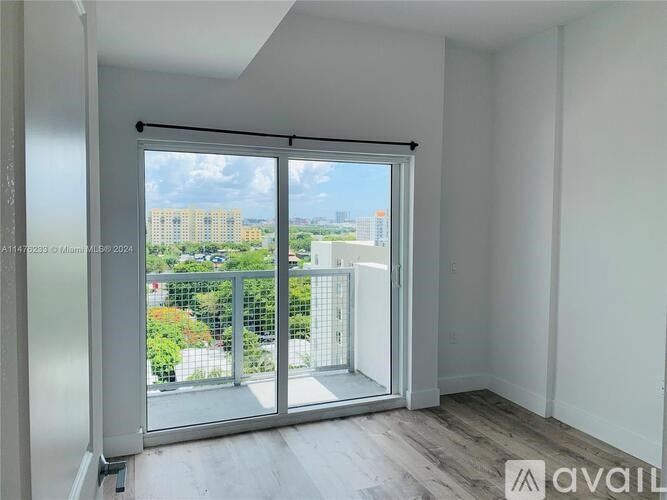 A room with a sliding glass door leading to a balcony with a view of buildings and greenery.