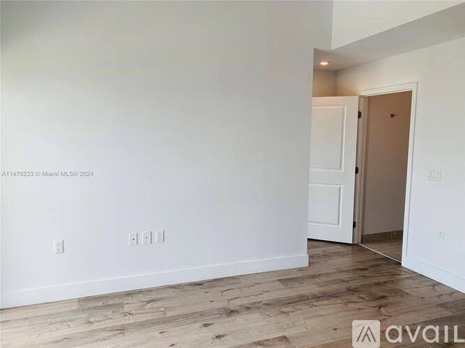 A room with white walls and wooden flooring, with a doorway leading to another room.