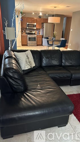 A black leather couch in a living room with a kitchen in the background.