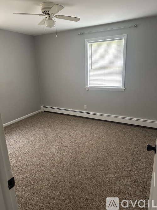 A room with a carpeted floor, a ceiling fan, and a window with blinds.
