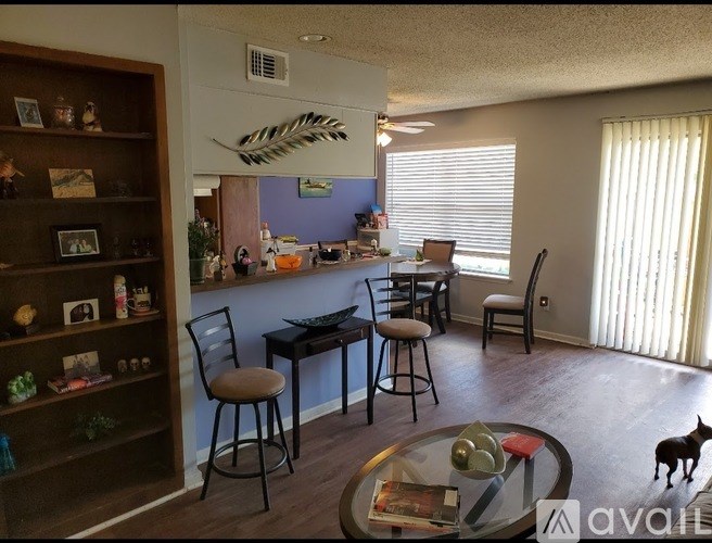 A dog is standing on a glass table in a room with a bar and chairs.