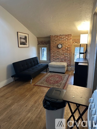 A living room with a black couch and a brick wall.