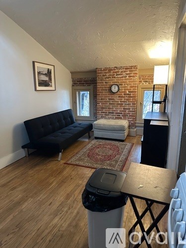 A living room with a black couch and a brick wall.