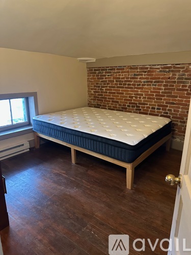 A bed with a white mattress and a blue cover is in a room with wooden floors and a brick wall.