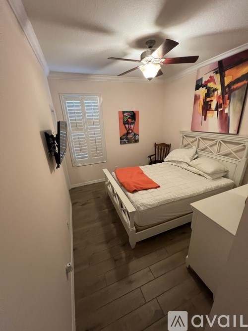 A bedroom with a bed, a ceiling fan, and a painting on the wall.
