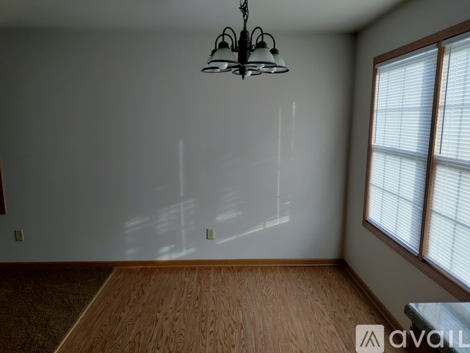 A room with a chandelier, wooden floor, and a window with blinds.