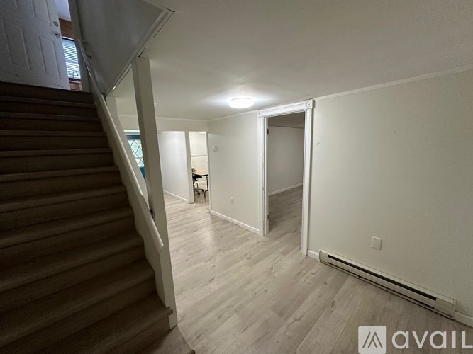 A room with wooden floors and white walls, with a staircase on the left side.