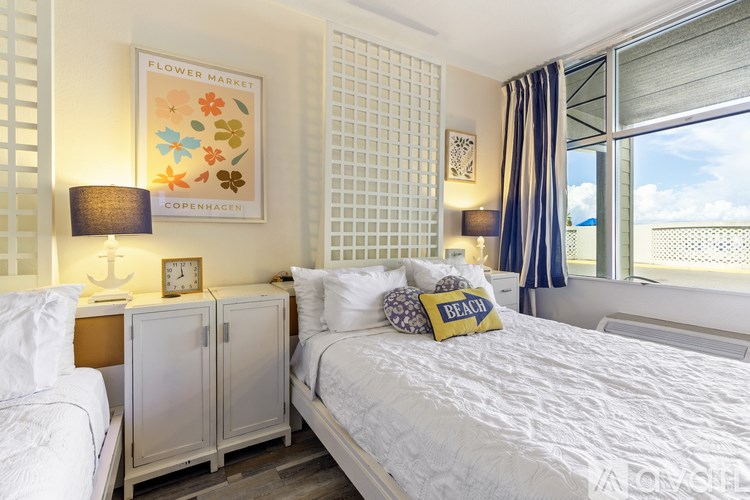 A bedroom with a large bed, a poster on the wall, and a window with a view of the city.