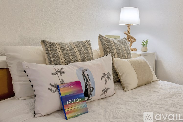 A bed with a white comforter and a book titled "Art Now" on it.