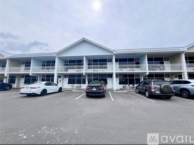 A parking lot in front of a white building with several cars parked.