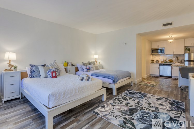A bedroom with two beds and a kitchen area in the background.