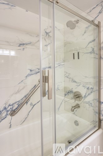 A shower with a glass door and a marble wall.